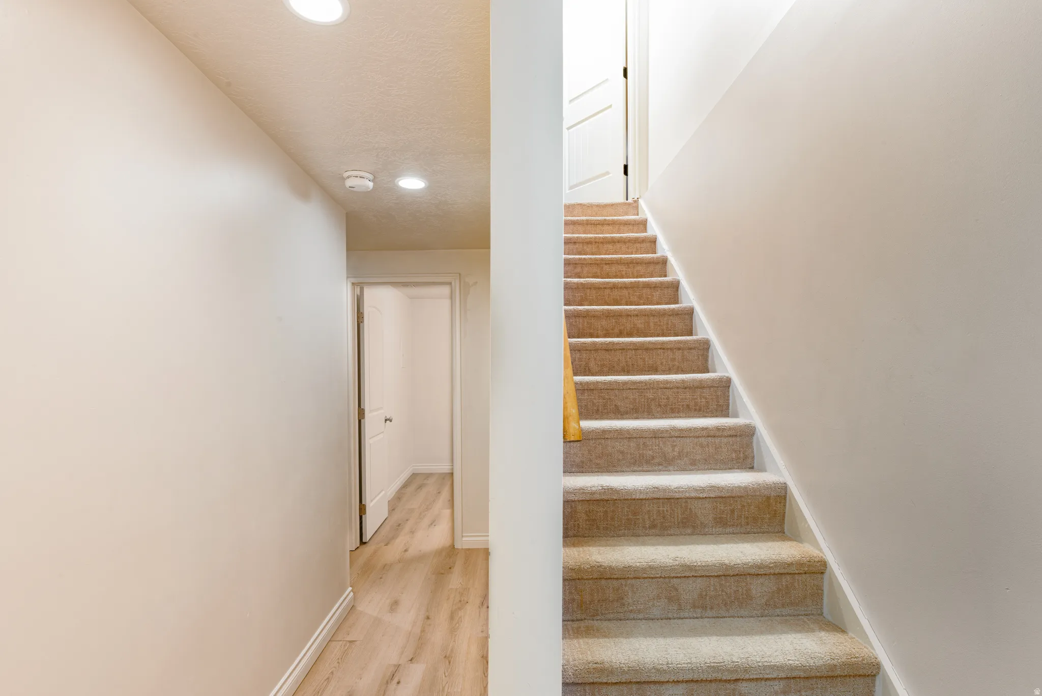 Stairway with recessed lighting and wood looking floors.