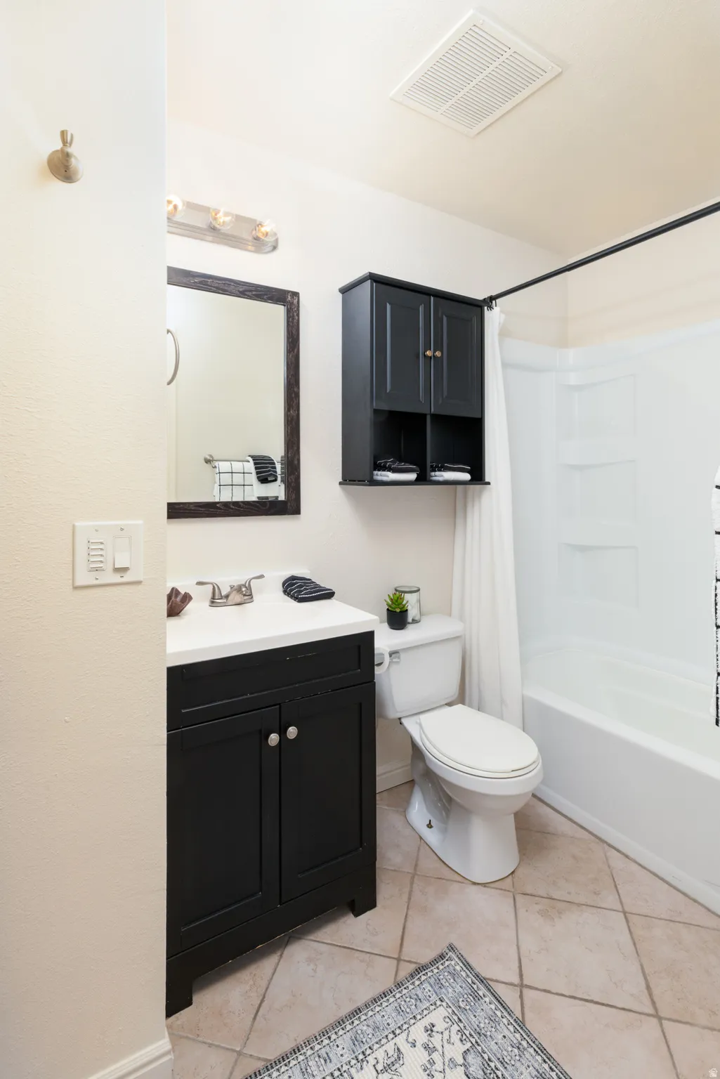 Bathroom with vanity, shower / bath combo with shower curtain, and light tile patterned floors.