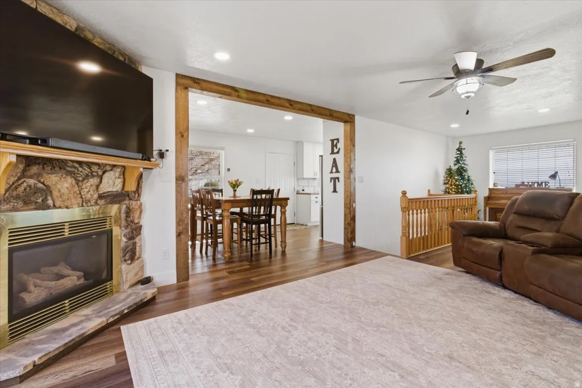 Living room featuring a ceiling fan, dark wood-style flooring, a stone fireplace, and recessed lighting