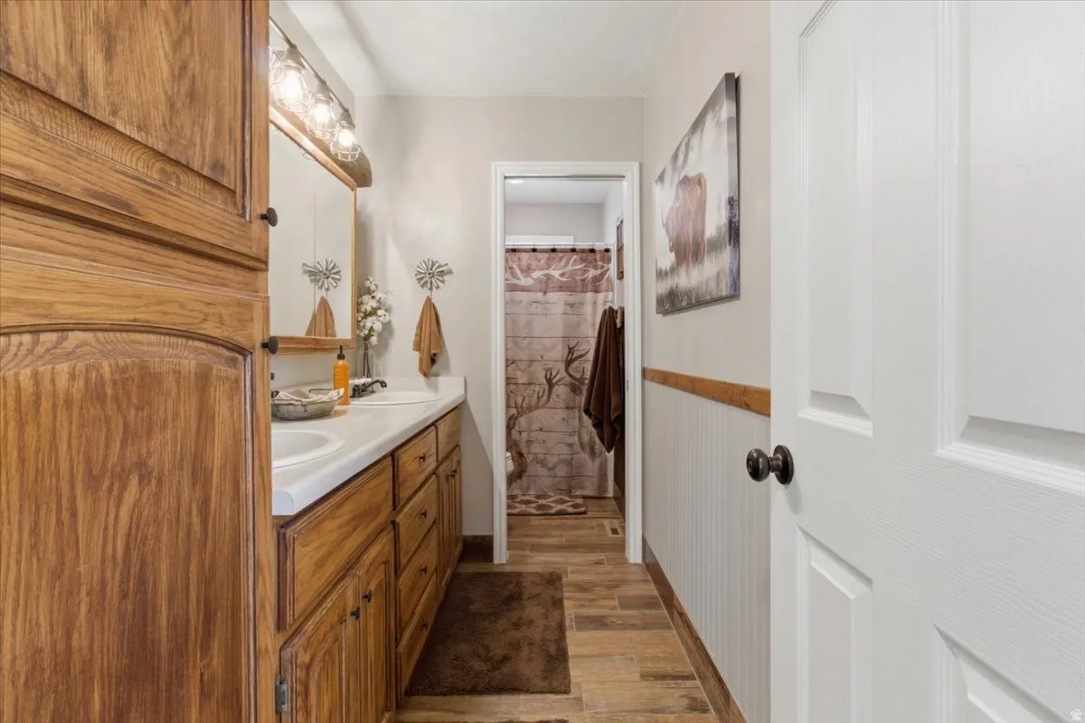 Bathroom with double vanity, a shower with shower curtain, and dark wood finished floors