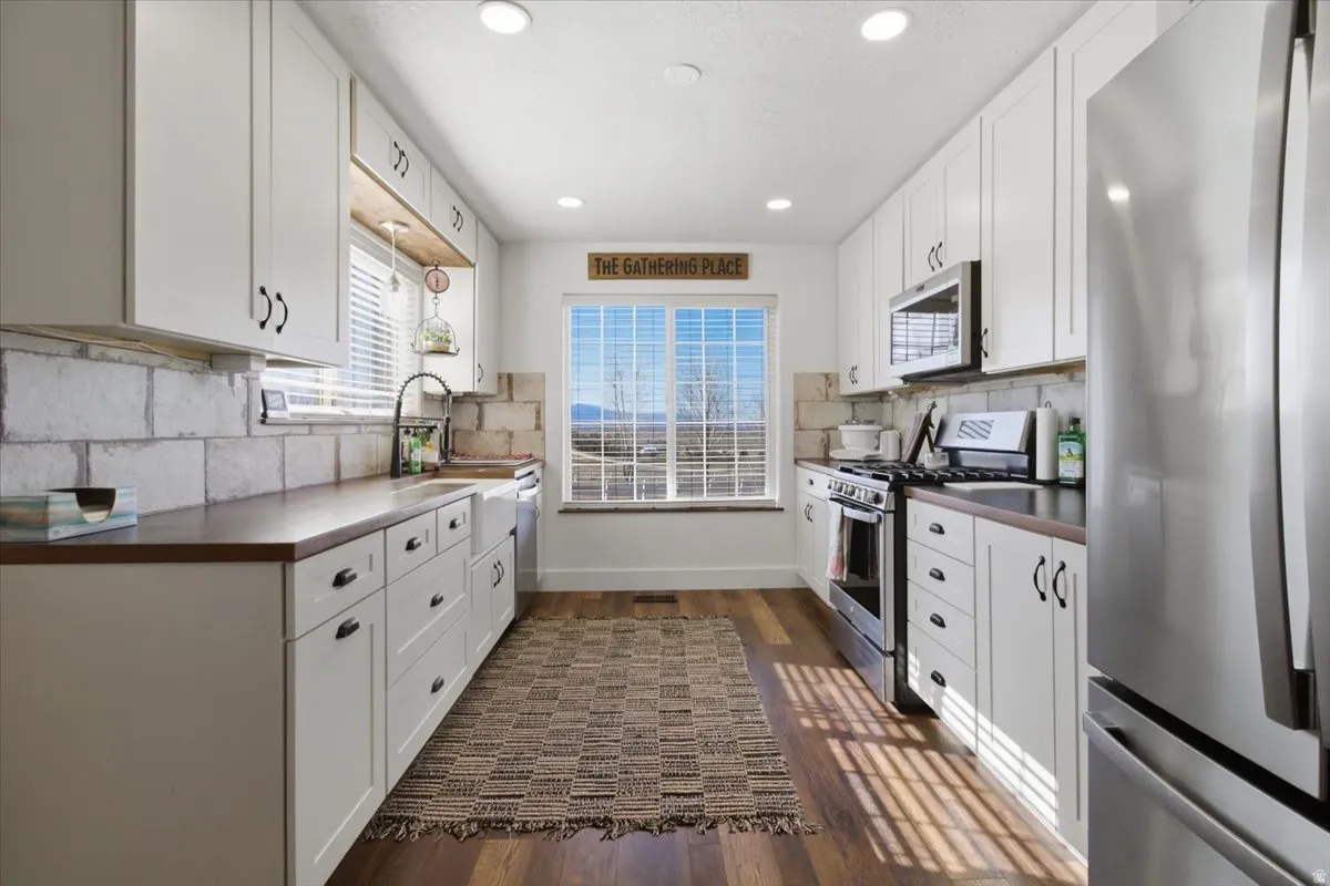 Kitchen featuring stainless steel appliances, dark countertops, white cabinets, dark wood-style flooring, and recessed lighting