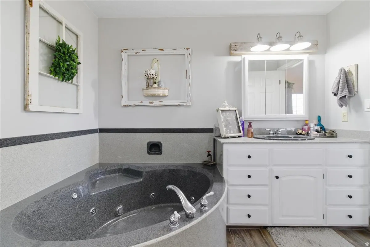 Full bath featuring vanity, a tub with jets, and wood finished floors