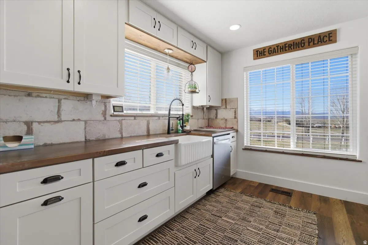 Kitchen with white cabinets, butcher block counters, dark wood finished floors, dishwasher, and backsplash