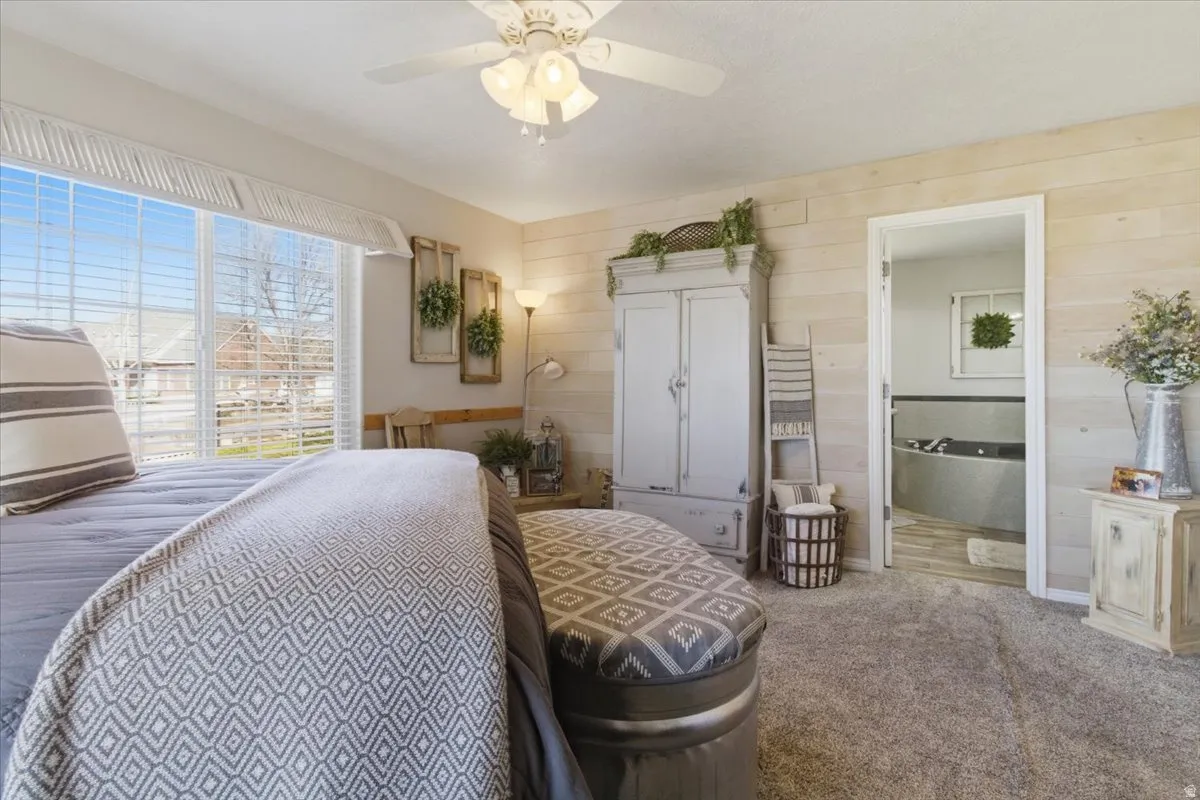 Carpeted bedroom with ensuite bath, a ceiling fan, and wood walls