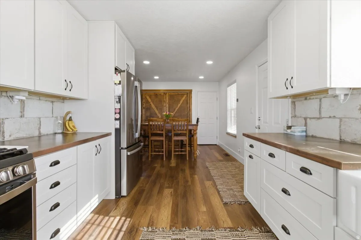 Kitchen with tasteful backsplash, white cabinets, stainless steel appliances, dark wood-style flooring, and recessed lighting