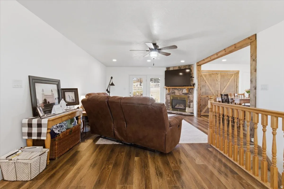 Living area with wood finished floors, a ceiling fan, and a stone fireplace
