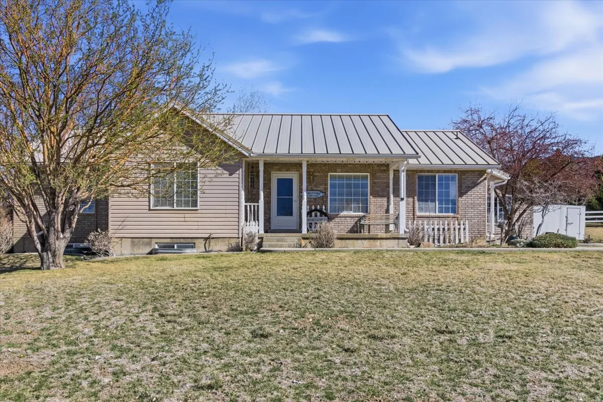 Ranch-style house with a porch, brick siding, a standing seam roof, and a front yard