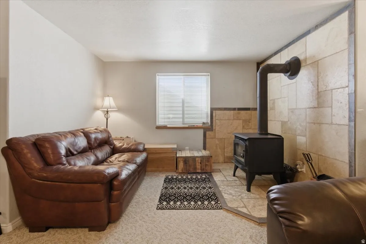 Carpeted living area with tile walls, a wood stove, a textured ceiling, and a wainscoted wall