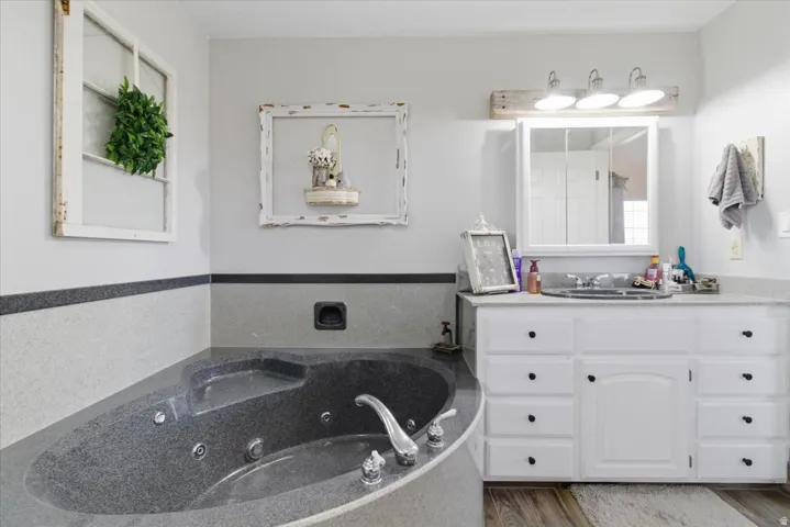 Full bath featuring vanity, a tub with jets, and wood finished floors