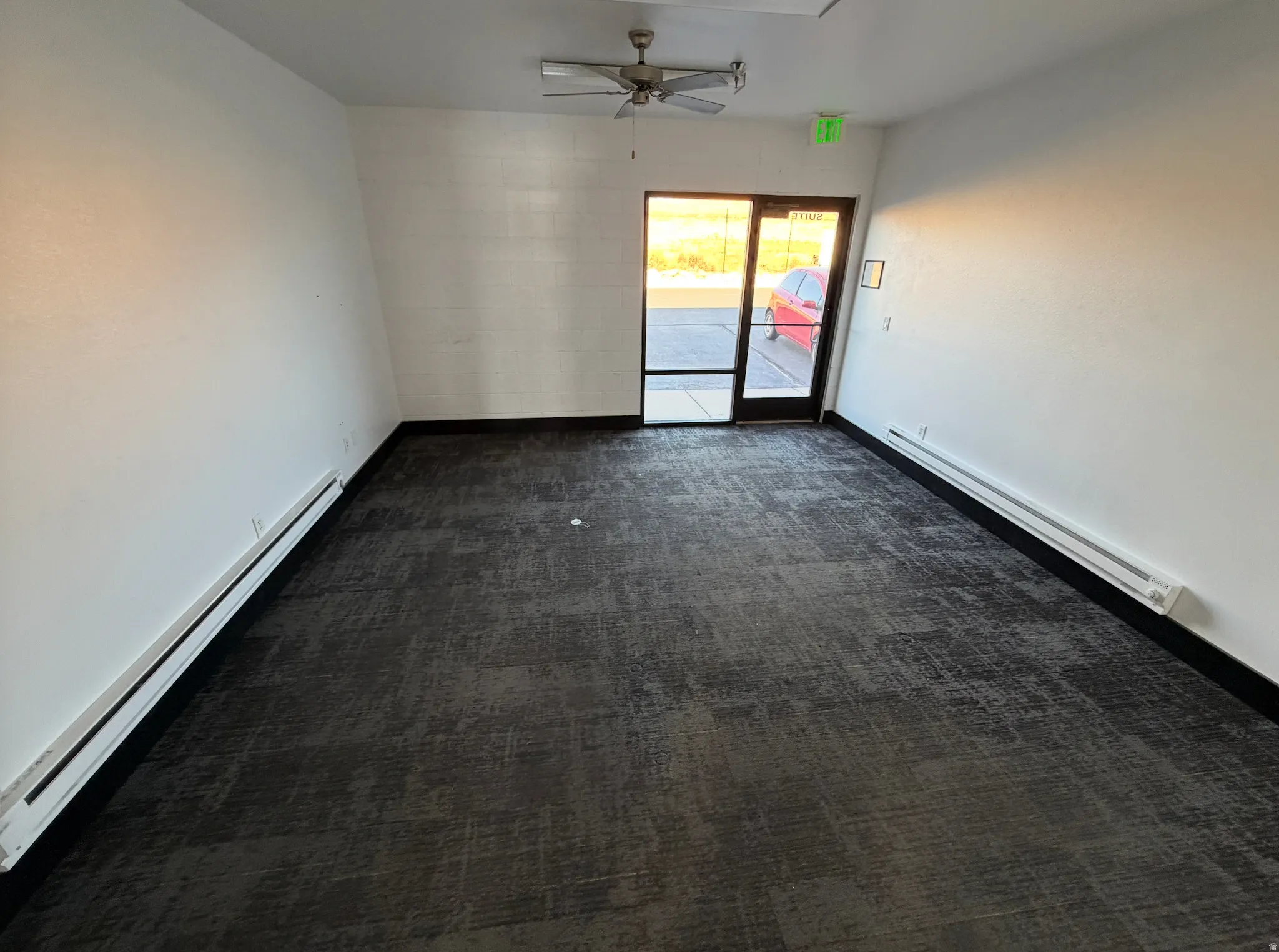 Empty room featuring a baseboard radiator, dark carpet, and ceiling fan