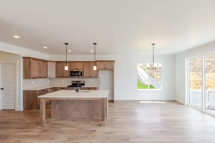 Open-concept kitchen and living area featuring wood-finish flooring, a kitchen island with sink and pendant lighting, stainless steel appliances, and sliding glass doors leading to an exterior deck