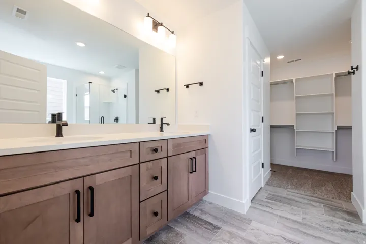 Bathroom featuring a dual vanity with light wood-finish cabinetry, white countertops, and matte black fixtures