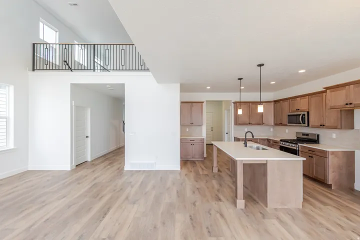 Open-concept living space featuring wood-finish flooring and a kitchen with light wood cabinetry, a center island with sink, stainless steel appliances, and pendant lighting