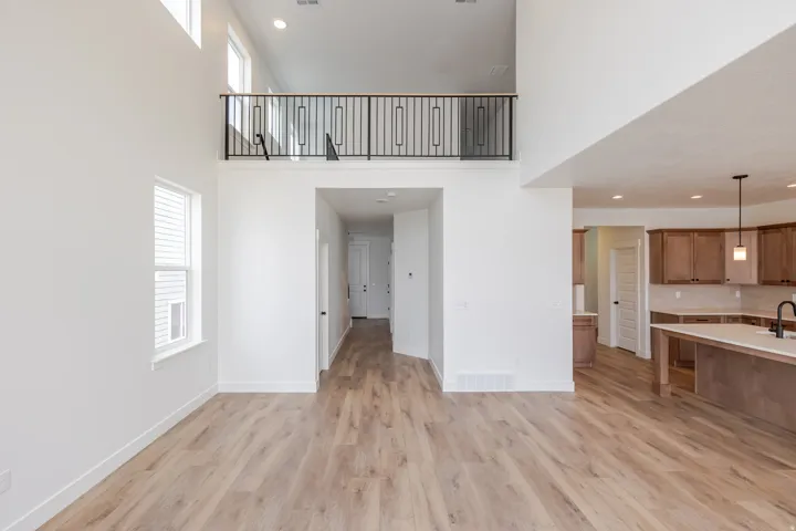 Spacious open-concept living area featuring wood-finish flooring, high ceilings, and a second-story interior balcony with a decorative metal railing