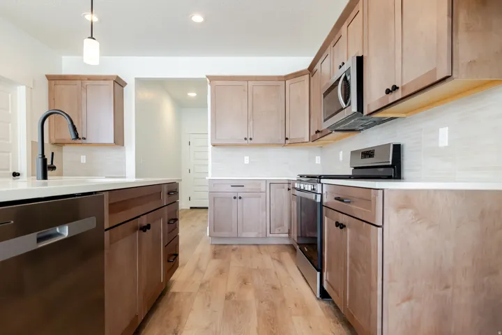 Modern kitchen featuring wood-finish flooring, light wood cabinetry, white countertops, and a tiled backsplash