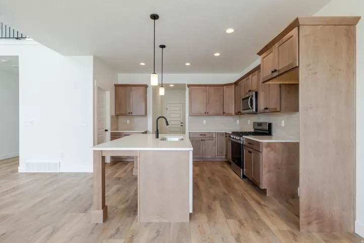 Spacious kitchen featuring an island with a white countertop and seating area, wood-finish flooring, recessed lighting, and stainless steel appliances
