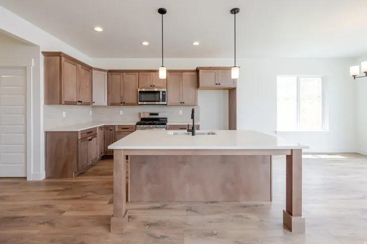 Kitchen featuring an island with a built-in sink, stainless steel microwave, gas range, wood-finish flooring, and pendant lighting