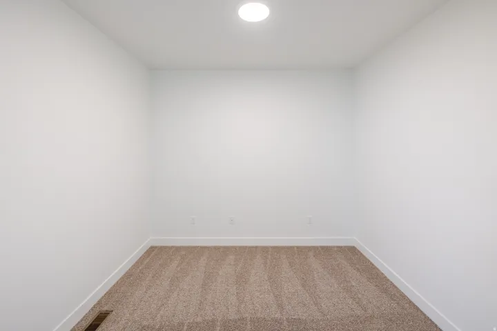 Room with light brown carpet flooring, white walls, and a recessed ceiling light
