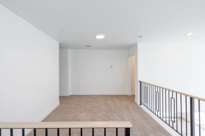 Carpeted landing area featuring a modern black metal railing with a wood-finish handrail, recessed lighting, and crisp white walls
