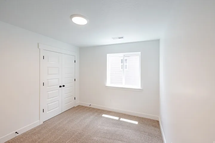 Carpeted room featuring a double-door closet with black hardware, a window with white trim, white walls, and a ceiling light fixture