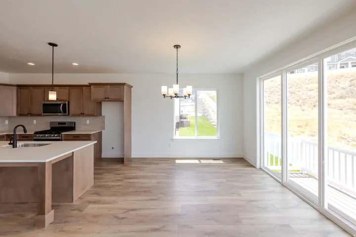 Open-concept kitchen and dining area featuring wood-finish flooring, a kitchen island with integrated sink, stainless steel appliances, and sliding glass doors to the exterior deck