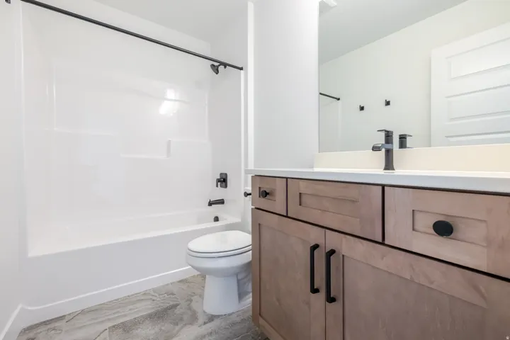 Bathroom featuring a white tub/shower combination with matte black fixtures, a contemporary vanity with light wood-finish cabinetry, a white countertop, and a sleek mirror