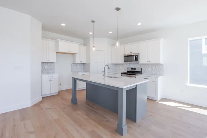 Open-concept kitchen featuring wood-finish flooring, white cabinetry, hexagon tile backsplash, stainless steel appliances, and a central island with a sink and pendant lighting