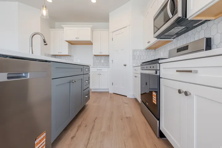 Modern kitchen featuring stainless steel appliances, wood-finish flooring, white cabinetry, a gray kitchen island, and a geometric tile backsplash