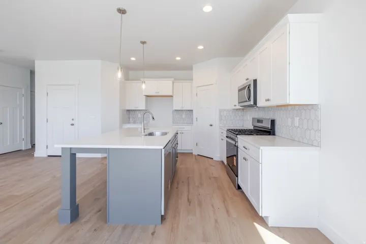 Kitchen featuring a central island with a quartz countertop, stainless steel appliances, white cabinetry, a geometric tile backsplash, and wood-finish flooring