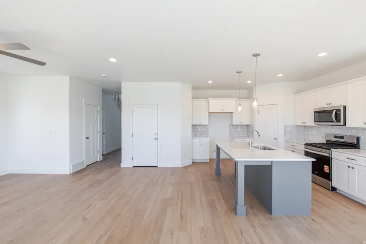 Open-concept kitchen with white cabinetry, stainless steel appliances, and a central island with a sink