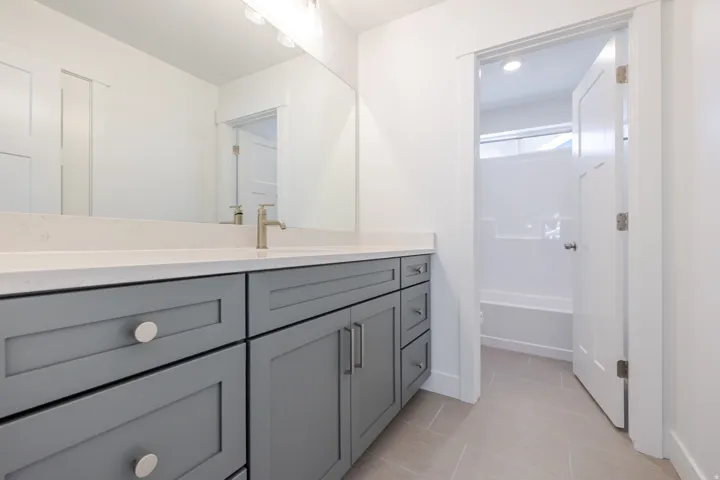 Extended vanity with gray shaker-style cabinetry, white solid surface countertop, and a single basin with a gold-finish faucet