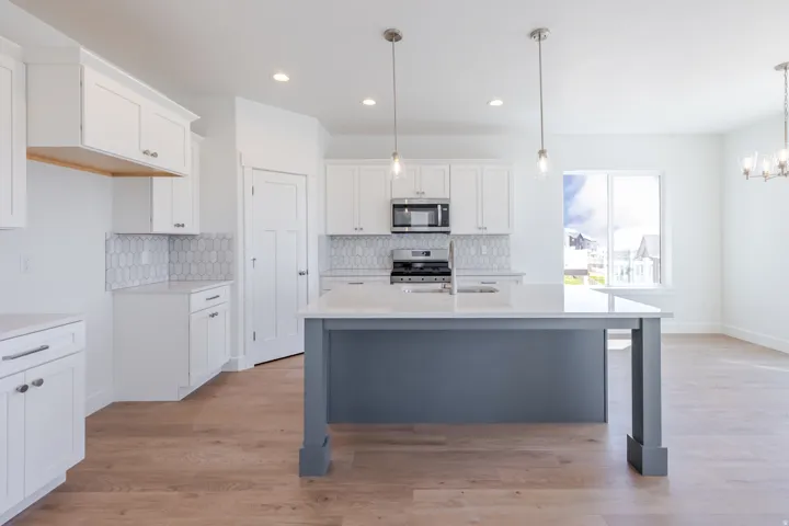 Open-concept kitchen featuring an island with a light-toned countertop, wood-finish flooring, white cabinetry, and a patterned tile backsplash