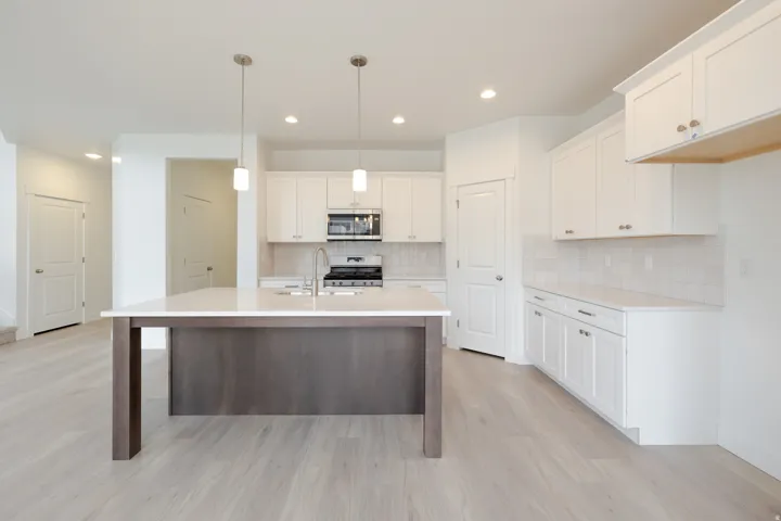Kitchen featuring a central island with white countertop, white shaker cabinetry, stainless steel appliances, subway tile backsplash, and light wood-finish flooring