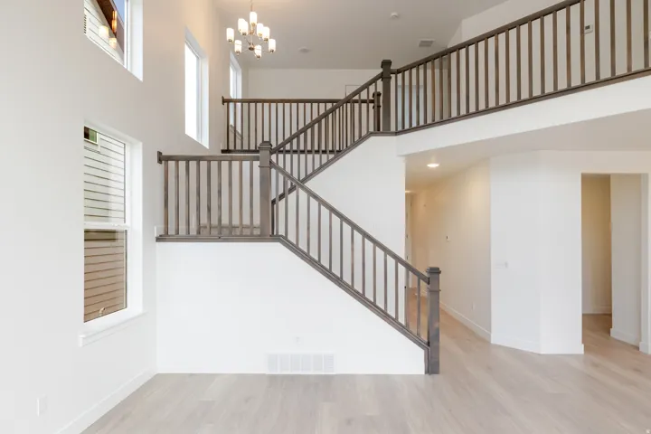 Two-story foyer featuring a grand staircase with dark wood-finish railings, high ceilings, multiple windows, and wood-finish flooring