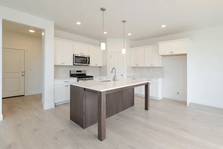 Open-concept kitchen featuring an island with a sink and pendant lighting, white cabinetry, a subway tile backsplash, stainless steel appliances, and wood-finish flooring