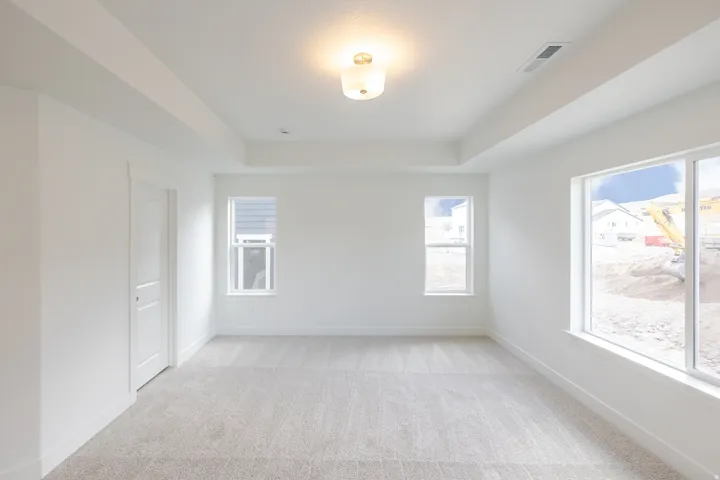 Bright interior space featuring a tray ceiling with a flush-mount light fixture, light-colored carpet flooring, white walls, and multiple windows