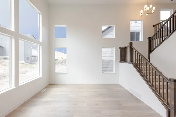 Two-story living area featuring multiple windows, wood-finish flooring, a contemporary chandelier, and a prominent staircase with dark wood newel posts and railings
