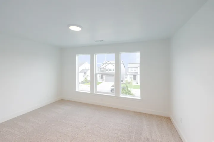 Bright room with three large windows, recessed ceiling light, white walls, and beige carpet flooring