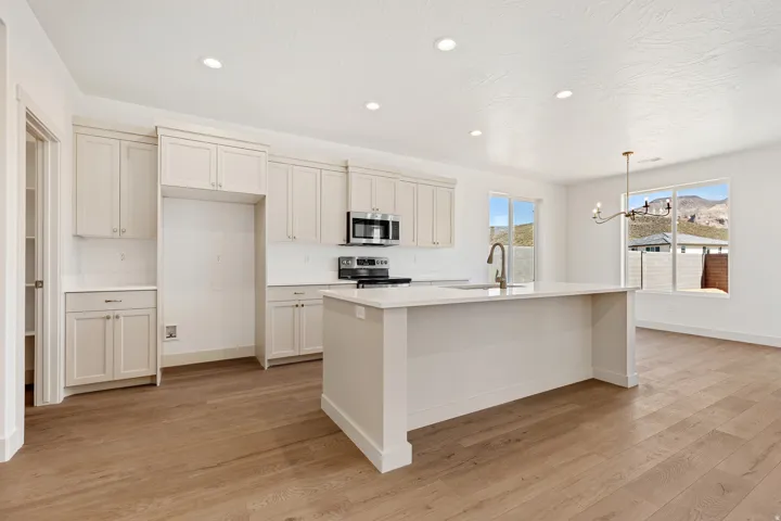 Kitchen featuring light wood-style floors, hanging lights, stainless steel appliances, and a kitchen island with sink