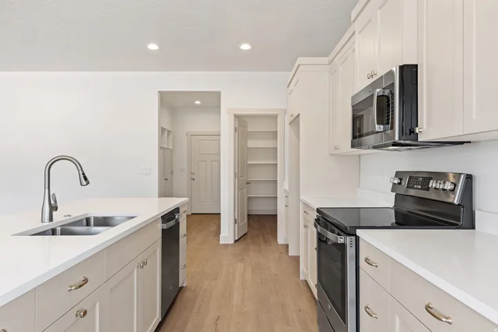 Kitchen featuring stainless steel appliances, light wood finished floors, light stone countertops, recessed lighting, and white cabinets