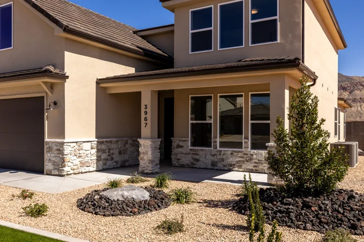 View of front facade with a porch, stone siding, stucco siding, and a garage