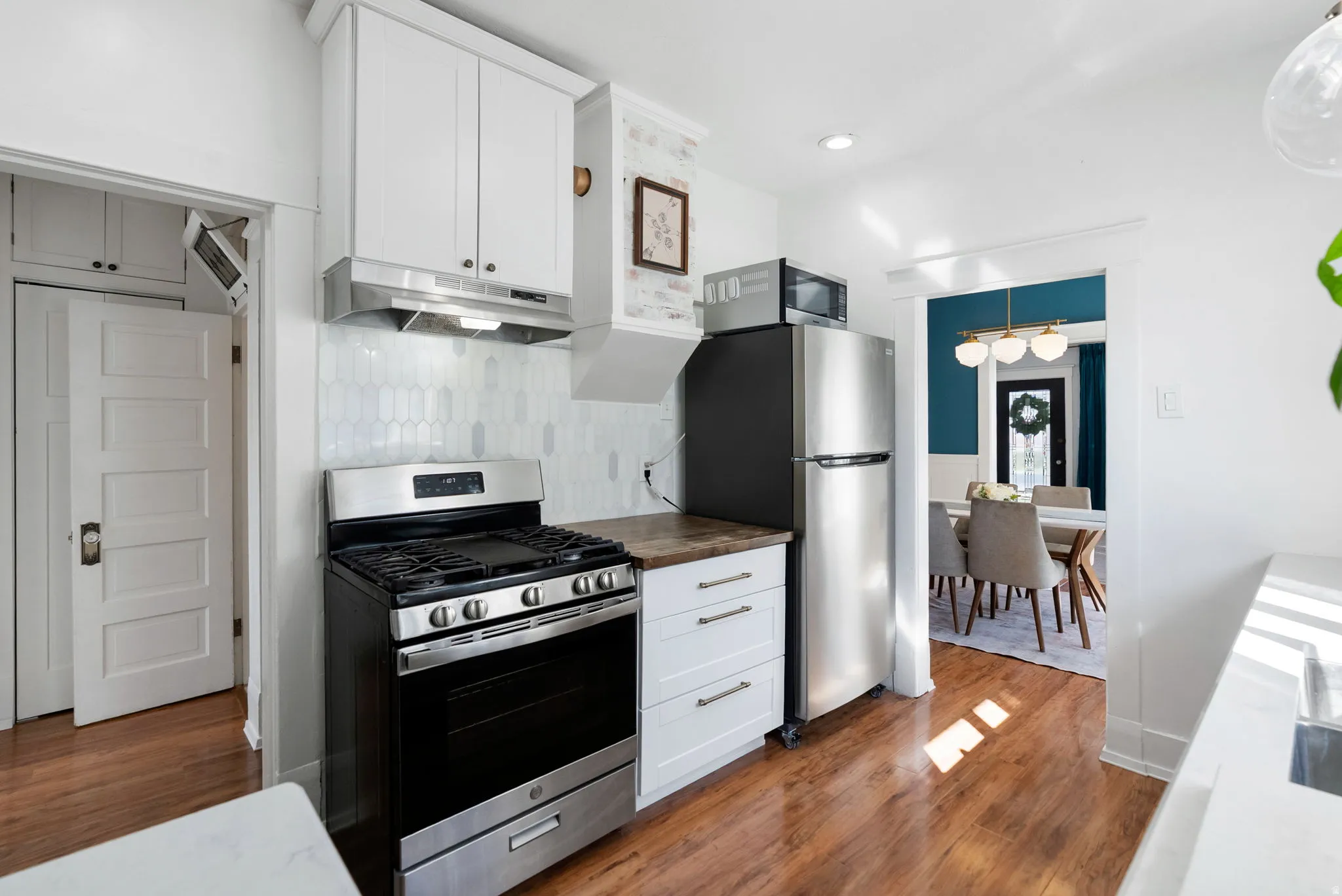 Kitchen with stainless steel appliances, white cabinetry, decorative backsplash, and dark wood-style floors