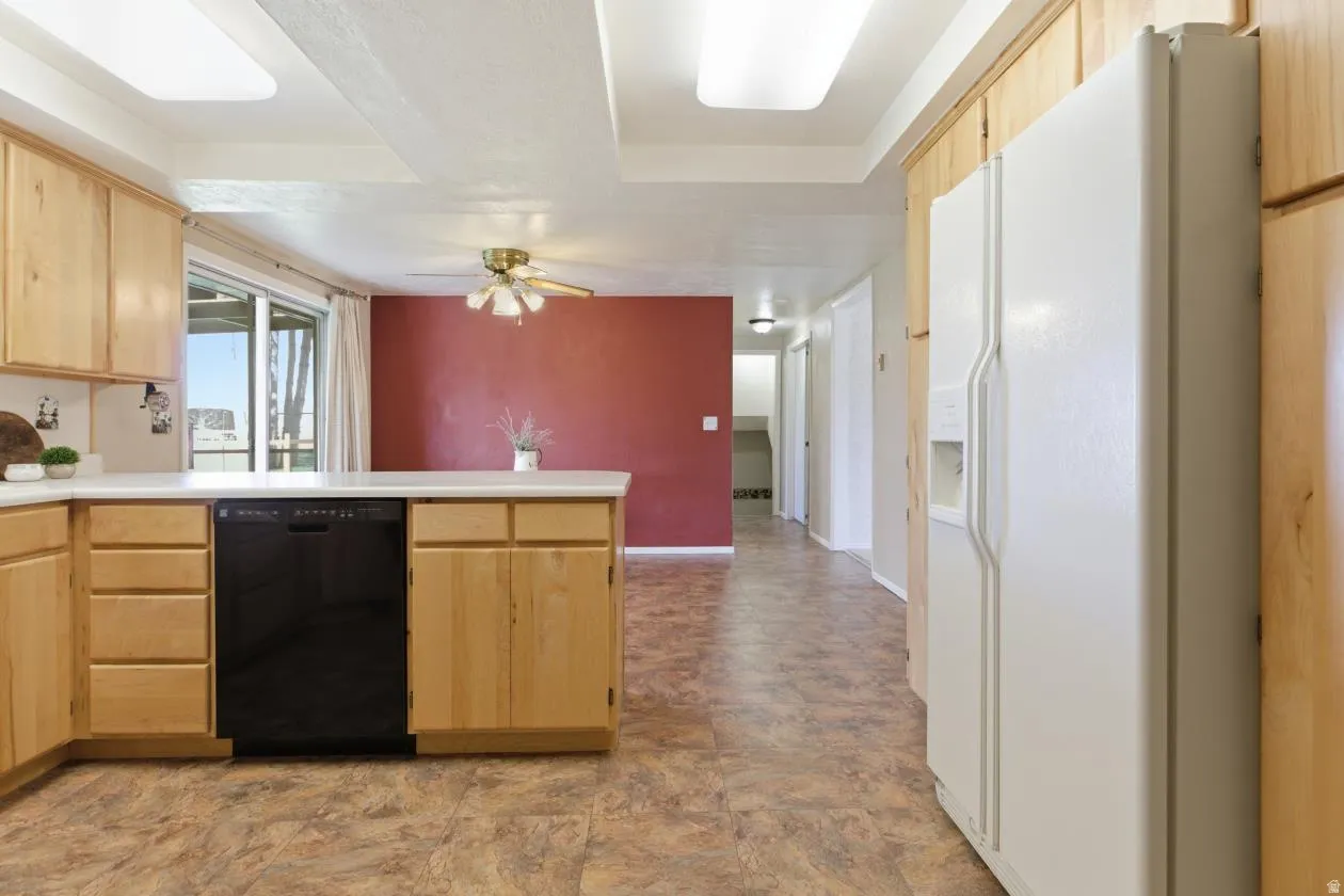 Kitchen with light wood finish cabinets, a peninsula, white refrigerator with ice dispenser, light countertops, and a raised ceiling