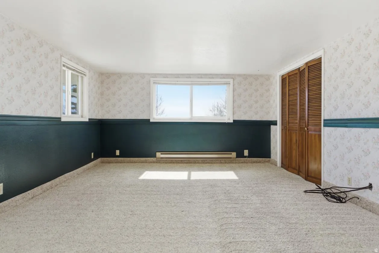 Spare room featuring wallpapered walls, wainscoting, carpet floors, and a baseboard radiator