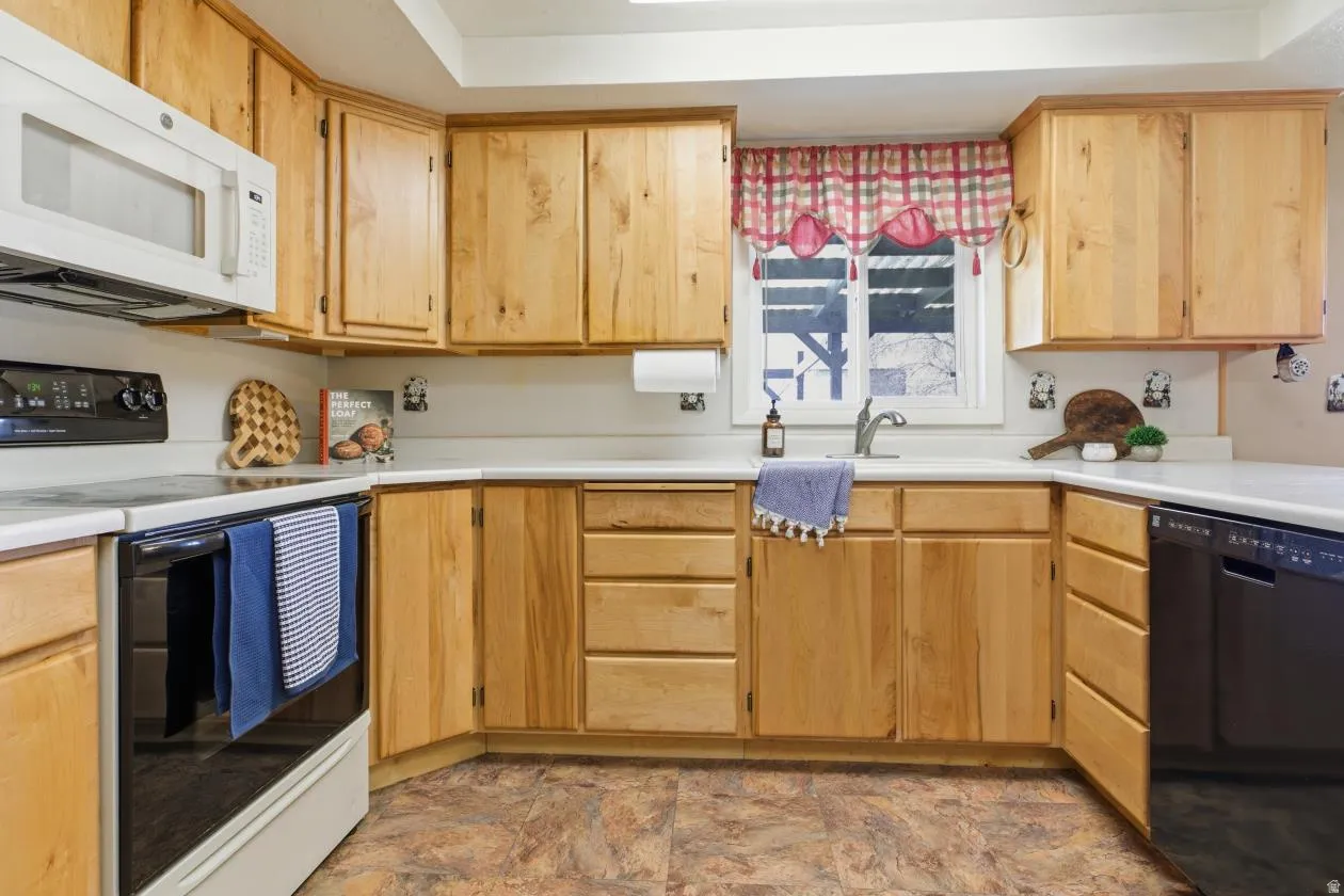Kitchen with range with electric cooktop, white microwave, dishwasher, light countertops, and a tray ceiling