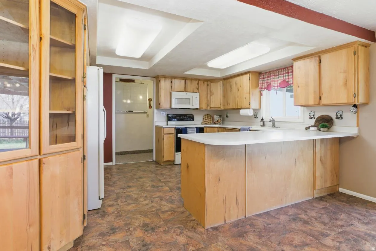Kitchen with a peninsula, light countertops, white appliances, and light wood finish cabinets