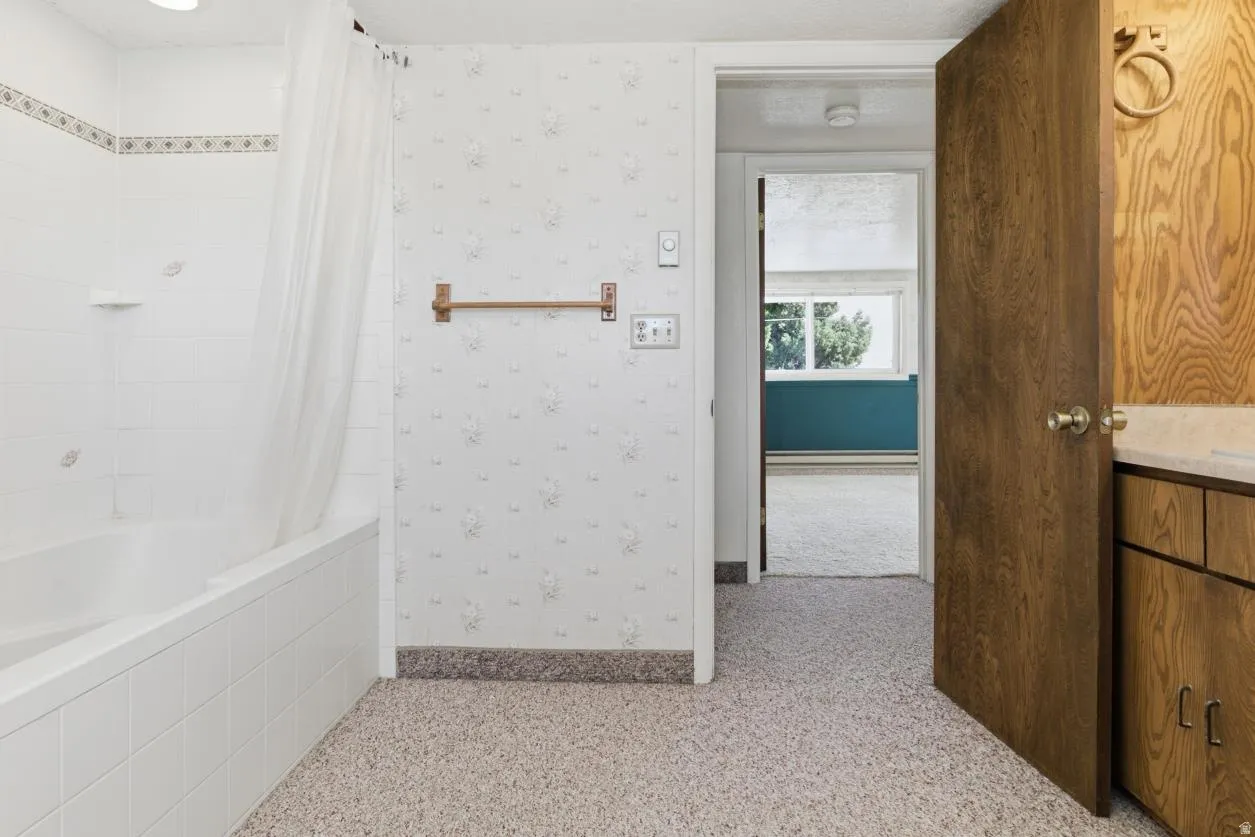 Bathroom featuring shower / bathtub combination with curtain, wallpapered walls, light colored carpet, and vanity