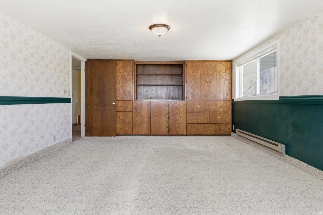 Empty room featuring wallpapered walls, baseboard heating, and light colored carpet