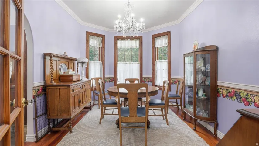 Dining area with wood finished floors, ornamental molding, hanging lights, and a wainscoted wall