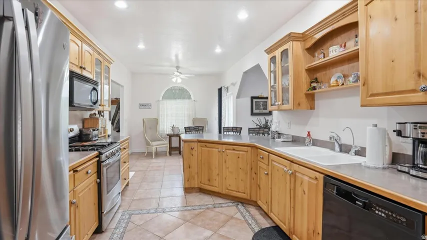 Kitchen with glass insert cabinets, inlaid floor details, black appliances, light tile patterned floors, and recessed lighting